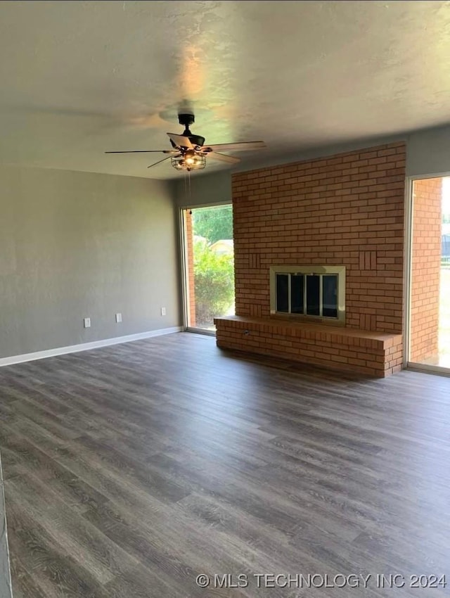 unfurnished living room with a brick fireplace, ceiling fan, and dark wood-type flooring