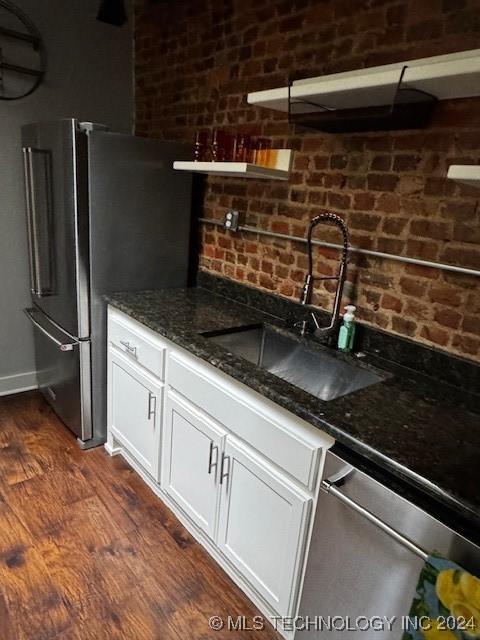 kitchen with dark wood-type flooring, dark stone counters, sink, white cabinetry, and stainless steel appliances