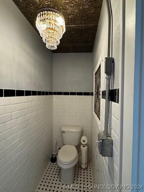 bathroom featuring toilet, tile walls, and a chandelier