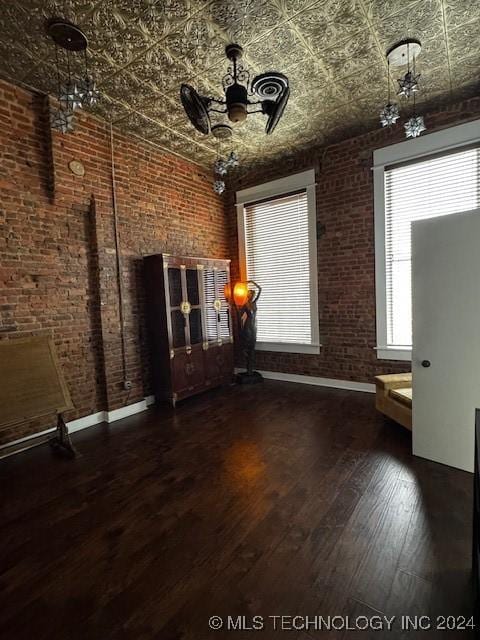 unfurnished room with dark hardwood / wood-style floors, ceiling fan, and brick wall