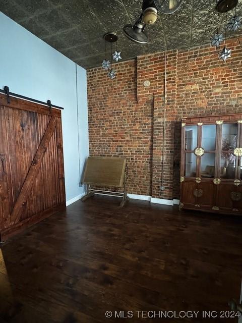 spare room with a barn door, dark hardwood / wood-style flooring, brick wall, and a high ceiling