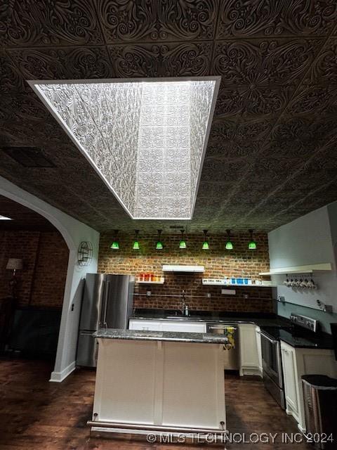 kitchen with wall chimney range hood, sink, appliances with stainless steel finishes, dark hardwood / wood-style flooring, and brick wall