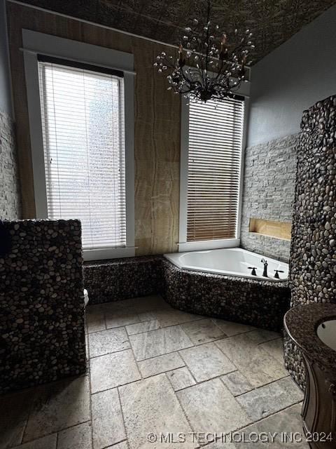 8 W Main St, Ardmore, OK 73401 - bathroom featuring a chandelier, stone tile floors, a relaxing tiled tub, and vanity