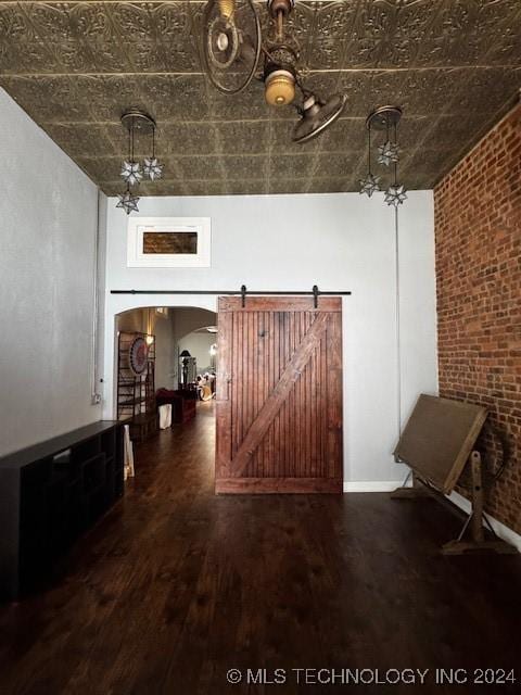 corridor featuring a barn door, dark hardwood / wood-style flooring, and brick wall