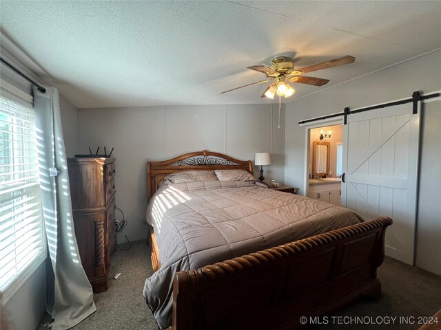 carpeted bedroom featuring ceiling fan, a barn door, a textured ceiling, and connected bathroom