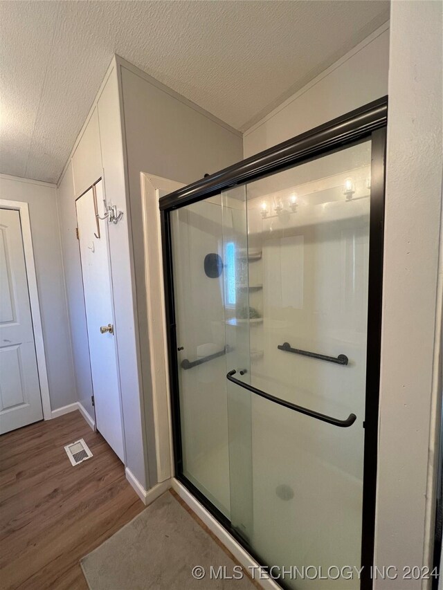 bathroom with hardwood / wood-style flooring, a shower with shower door, and a textured ceiling