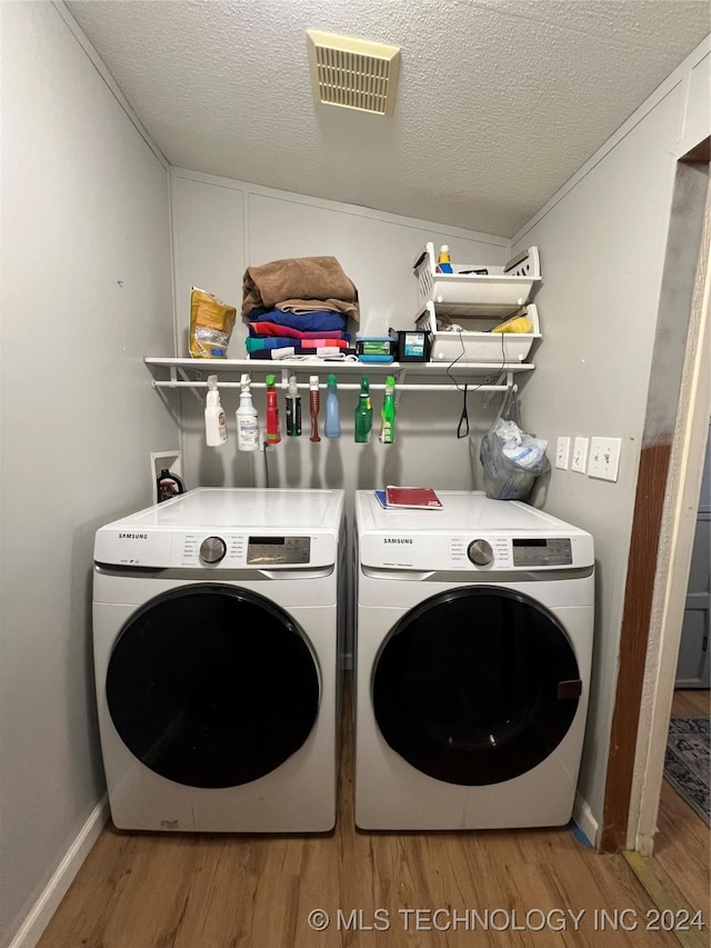 laundry area with a textured ceiling, light hardwood / wood-style floors, and washing machine and clothes dryer