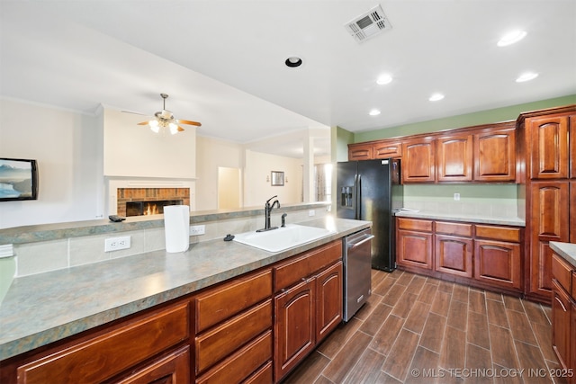 kitchen with sink, black refrigerator with ice dispenser, stainless steel dishwasher, ceiling fan, and a fireplace