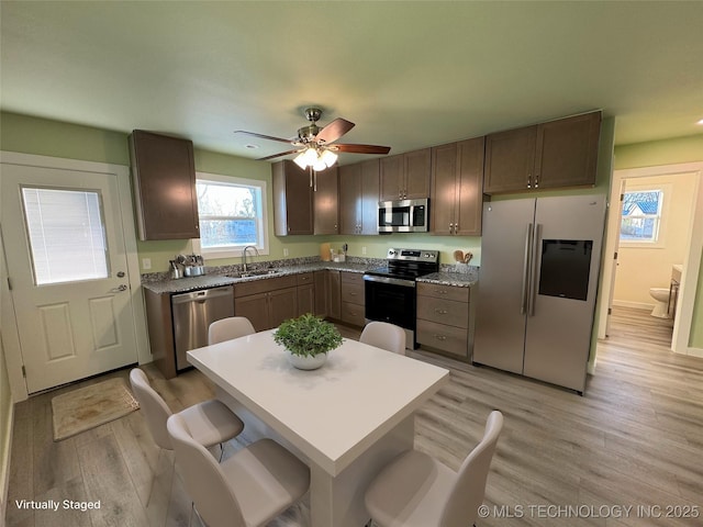 kitchen featuring ceiling fan, sink, stainless steel appliances, a kitchen breakfast bar, and light hardwood / wood-style floors