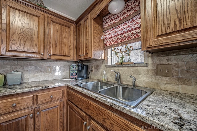 kitchen featuring backsplash, light stone counters, sink, and a textured ceiling