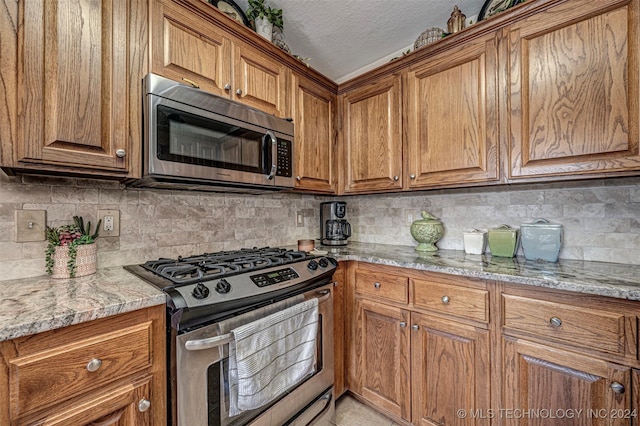 kitchen with light stone countertops, appliances with stainless steel finishes, a textured ceiling, and decorative backsplash