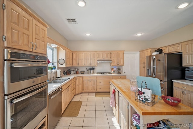 kitchen with appliances with stainless steel finishes, sink, wooden counters, light tile patterned floors, and light brown cabinets