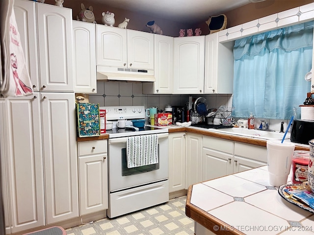 kitchen with tile countertops, white cabinets, sink, electric range, and decorative backsplash