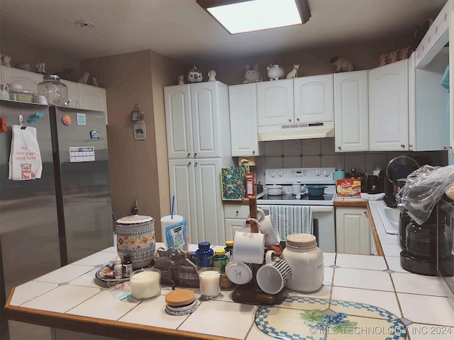 kitchen featuring white cabinets, tasteful backsplash, tile counters, range, and stainless steel refrigerator