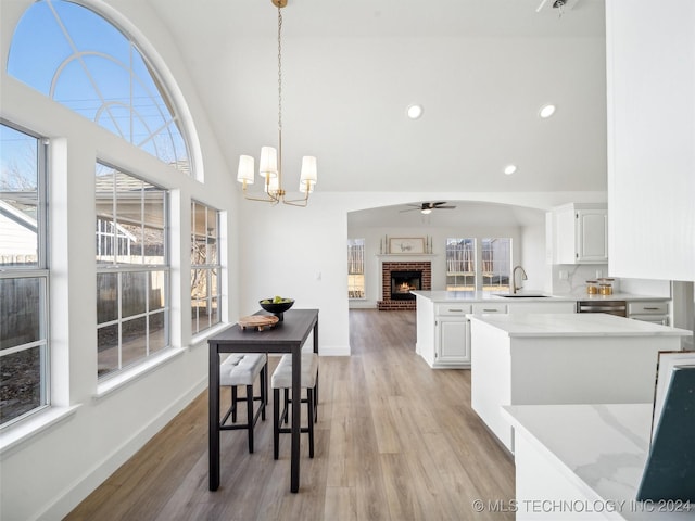 dining area featuring sink, light hardwood / wood-style flooring, high vaulted ceiling, a fireplace, and ceiling fan with notable chandelier