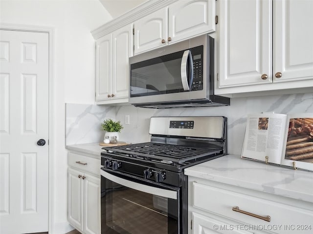 kitchen with light stone countertops, white cabinetry, backsplash, and appliances with stainless steel finishes