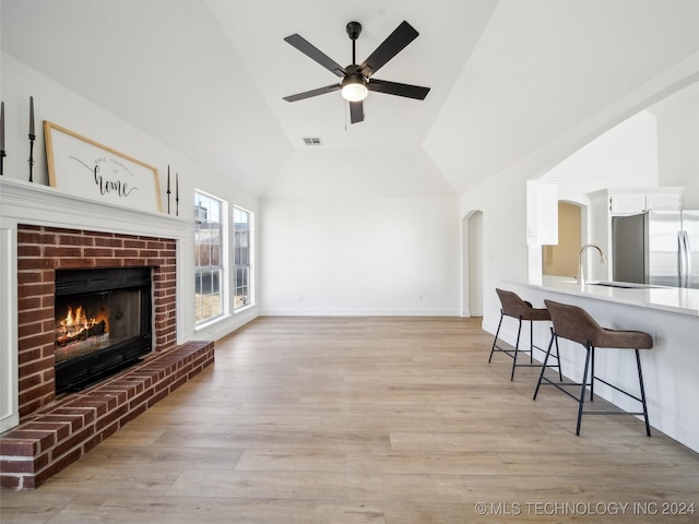 living room with ceiling fan, sink, light hardwood / wood-style floors, lofted ceiling, and a fireplace