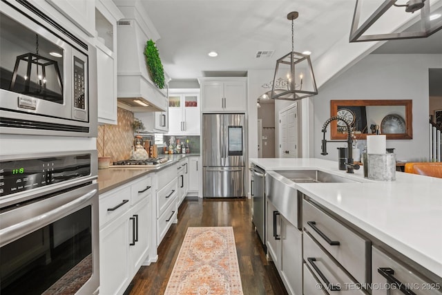 kitchen with pendant lighting, white cabinets, sink, appliances with stainless steel finishes, and custom range hood