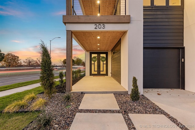 exterior entry at dusk with a garage, french doors, a balcony, and stucco siding