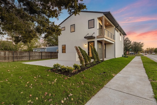 property exterior at dusk featuring a balcony and a lawn