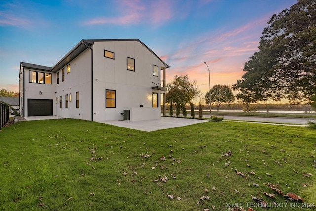 back house at dusk with a lawn, a patio, and a garage