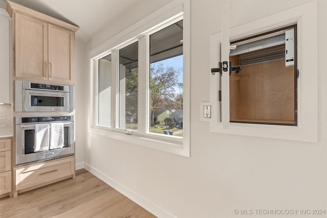 kitchen with plenty of natural light, light brown cabinets, light wood-type flooring, and double oven