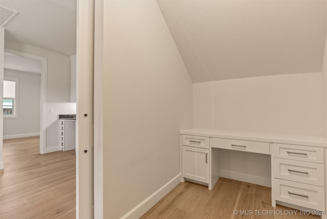 unfurnished office featuring light hardwood / wood-style floors, built in desk, and vaulted ceiling