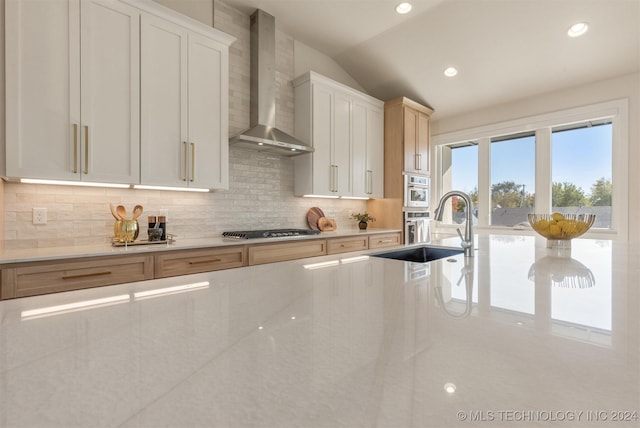 kitchen featuring lofted ceiling, white cabinets, wall chimney range hood, sink, and tasteful backsplash