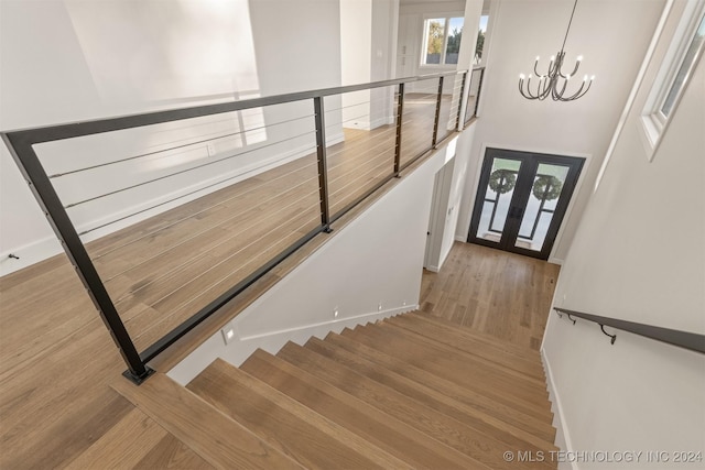 staircase with hardwood / wood-style floors, an inviting chandelier, and french doors