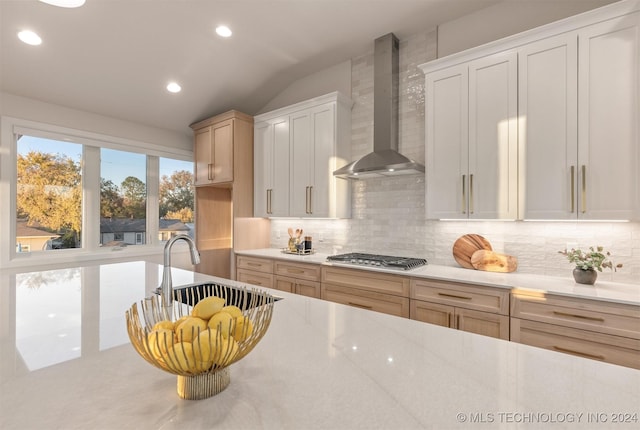 kitchen featuring backsplash, white cabinetry, wall chimney range hood, and stainless steel gas stovetop