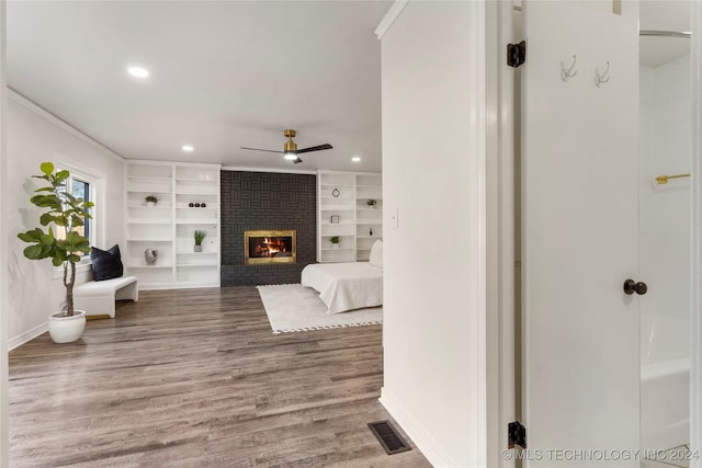 bedroom with hardwood / wood-style floors, a brick fireplace, ceiling fan, and crown molding