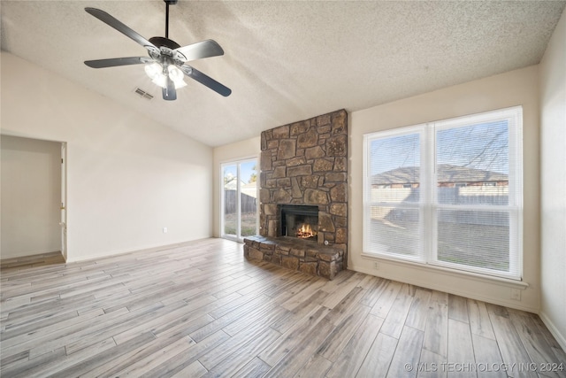 unfurnished living room with ceiling fan, a textured ceiling, lofted ceiling, a fireplace, and light wood-type flooring