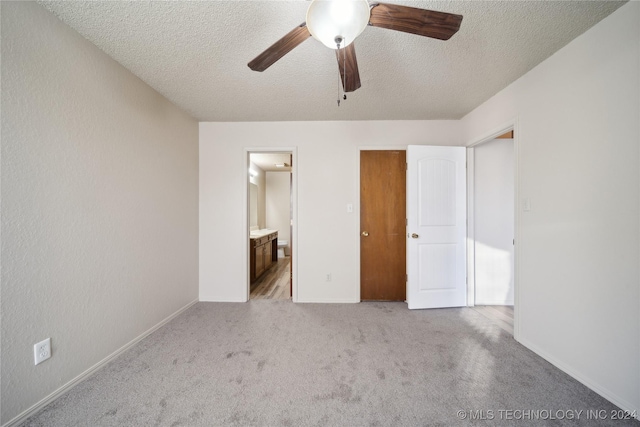 unfurnished bedroom featuring ceiling fan, light colored carpet, ensuite bathroom, and a textured ceiling