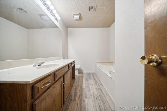 bathroom featuring wood-type flooring, a textured ceiling, toilet, a bathtub, and vanity