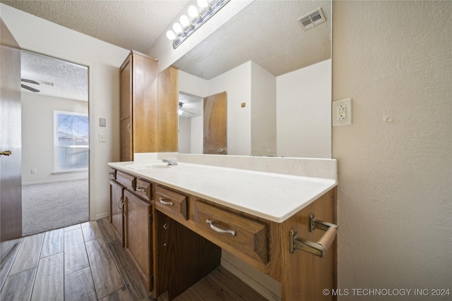 bathroom with ceiling fan, hardwood / wood-style floors, vanity, and a textured ceiling