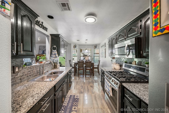 kitchen with tasteful backsplash, light stone counters, a textured ceiling, stainless steel appliances, and sink