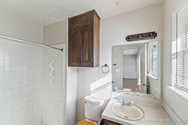 bathroom featuring a tile shower, vanity, and toilet