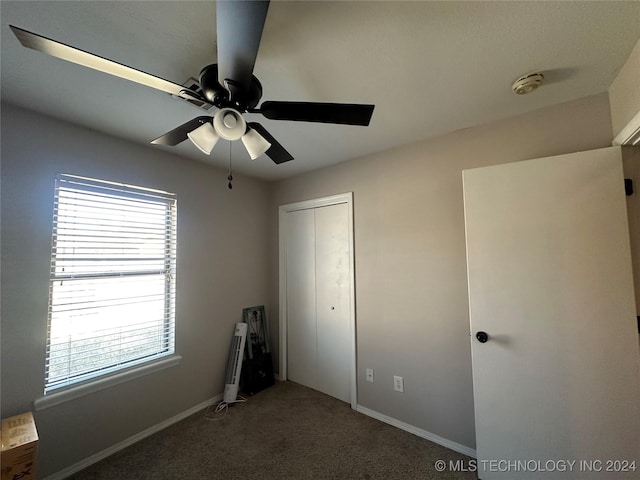 unfurnished bedroom featuring dark colored carpet, multiple windows, a closet, and ceiling fan