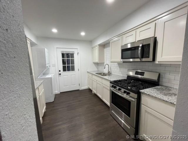kitchen featuring dark wood-style floors, a sink, decorative backsplash, stainless steel appliances, and white cabinets