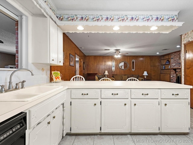 kitchen with white cabinetry, dishwasher, sink, kitchen peninsula, and wooden walls