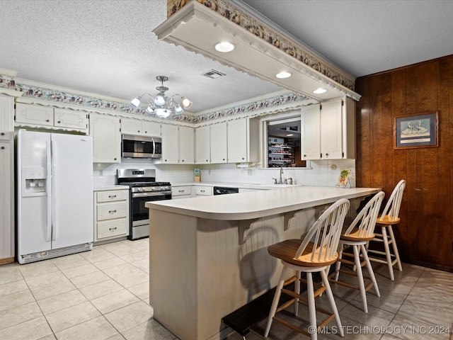 kitchen with wood walls, white cabinets, a textured ceiling, appliances with stainless steel finishes, and kitchen peninsula