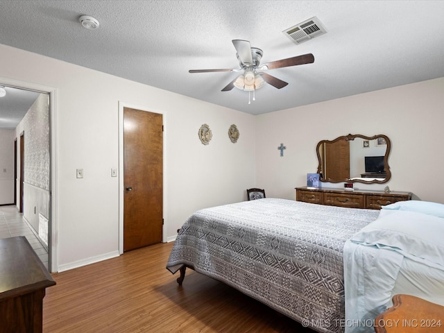 bedroom with ceiling fan, a textured ceiling, and light hardwood / wood-style flooring