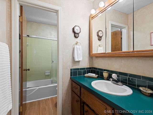 bathroom featuring backsplash, bath / shower combo with glass door, wood-type flooring, a textured ceiling, and vanity