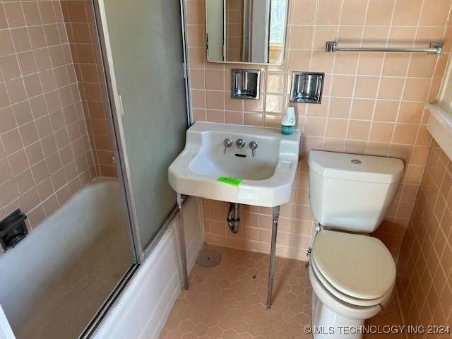 bathroom featuring toilet, tile patterned flooring, tile walls, and combined bath / shower with glass door