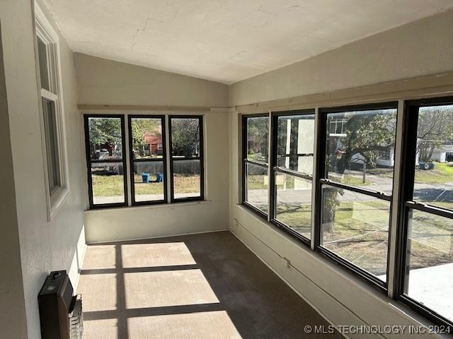 unfurnished sunroom featuring a healthy amount of sunlight, heating unit, and lofted ceiling