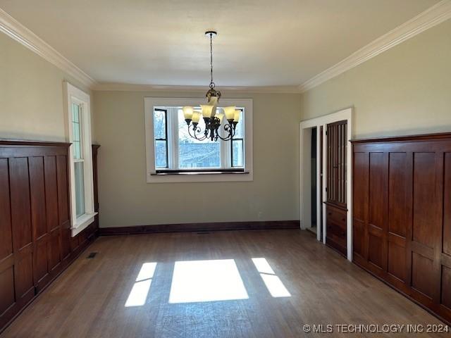 unfurnished dining area featuring a notable chandelier, ornamental molding, and dark wood-type flooring