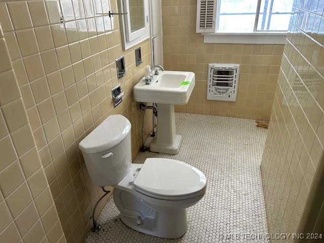 bathroom with sink, tile patterned flooring, heating unit, toilet, and tile walls