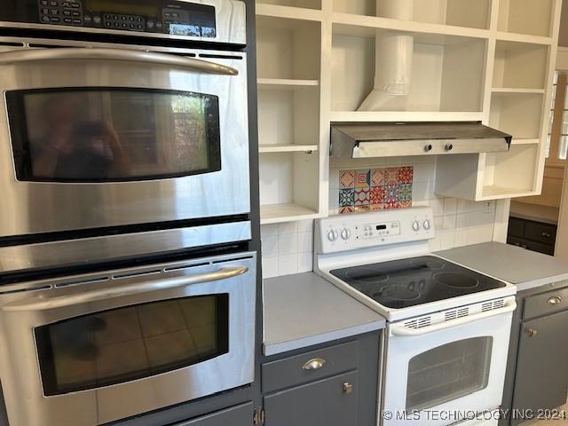 kitchen featuring backsplash, exhaust hood, white electric stove, gray cabinets, and double oven