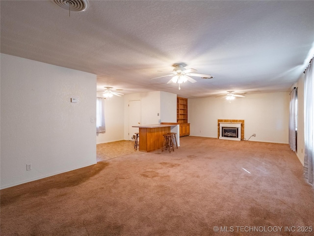 unfurnished living room with light carpet, a textured ceiling, a fireplace, and ceiling fan