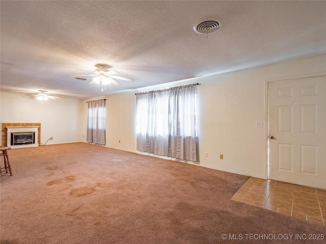 unfurnished living room featuring a tile fireplace, carpet, a textured ceiling, and ceiling fan